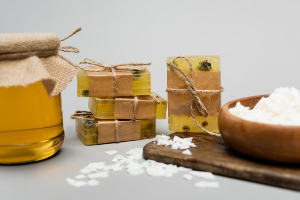 Handmade soap near blurred wax and jar with honey on cutting board on grey background - Photo, Image