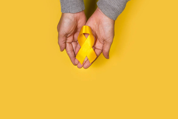 Man hands holding a yellow ribbon on a yellow background with copy space - 写真・画像