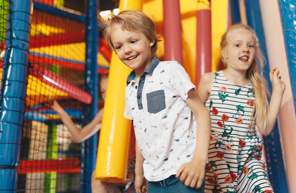 Szczęśliwego rodzeństwa bawiącego się w Play Centre. Chłopiec i dziewczęta biegający po szlaku skokowym. Zajęcia rekreacyjne dla dzieci w szkole - Zdjęcie, obraz
