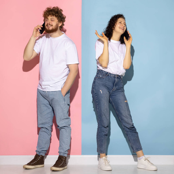 Portrait of young emotive man and girl using smartphones isolated on blue and pink trendy color background. Human emotions concept - Photo, image