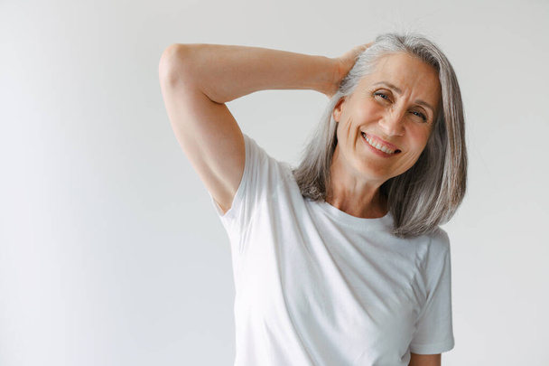 Grey senior woman in t-shirt smiling and looking at camera isolated over white background - Φωτογραφία, εικόνα