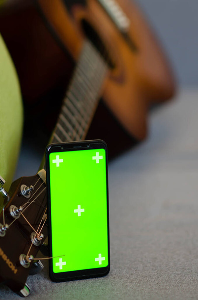 Selektiver Fokus auf Telefon mit Greenscreen von Chromakey-Mockup mit Tracking-Markierungen in der Nähe der Gitarre mit Kopierraum. Grüner Bildschirm und Chroma-Taste. Online-Gitarrenkurse. - Foto, Bild
