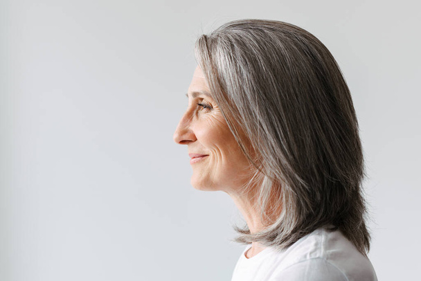 Grey senior woman in t-shirt smiling while posing in profile isolated over white background - Photo, Image