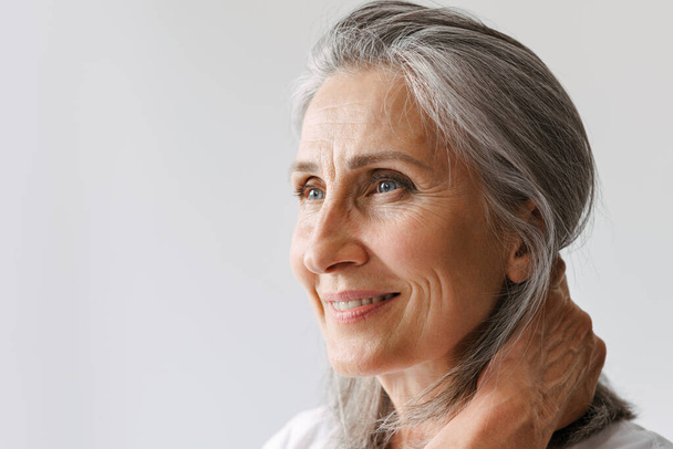 Grey senior woman in t-shirt smiling while looking aside isolated over white background - Foto, Imagem