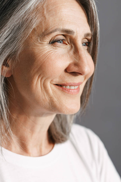 Mulher sênior branco em t-shirt sorrindo e olhando para o lado isolado sobre fundo cinza - Foto, Imagem