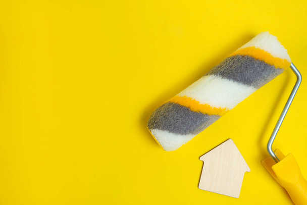 Paint roller for painting walls on a yellow background and a figurine of a house.Concept of home renovation - Photo, image