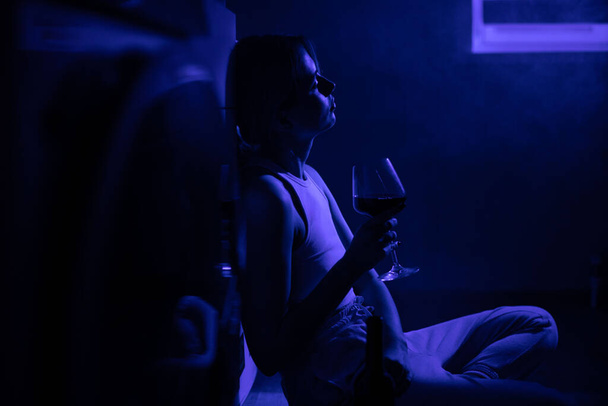 Sad woman drinking wine while sitting near the refrigerator in the dark. - Photo, Image