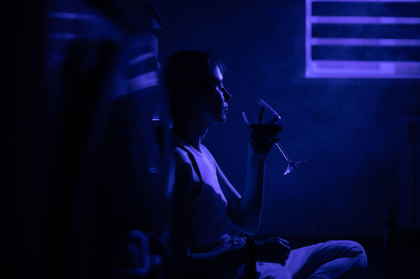 Sad woman drinking wine while sitting near the refrigerator in the dark. - Photo, image