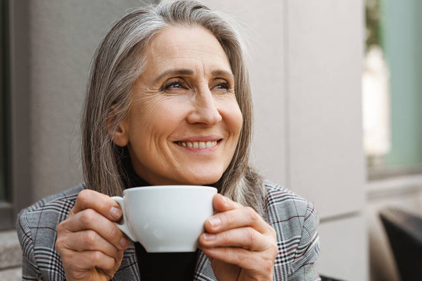 Grey white senior woman drinking coffee while sitting in cafe outdoors - Fotoğraf, Görsel