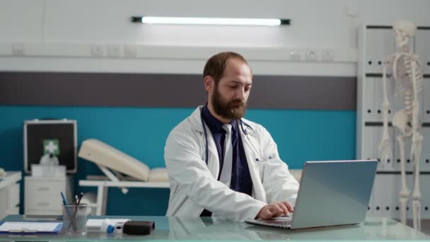 Portrait of male physician wearing white coat and using laptop - Footage, Video