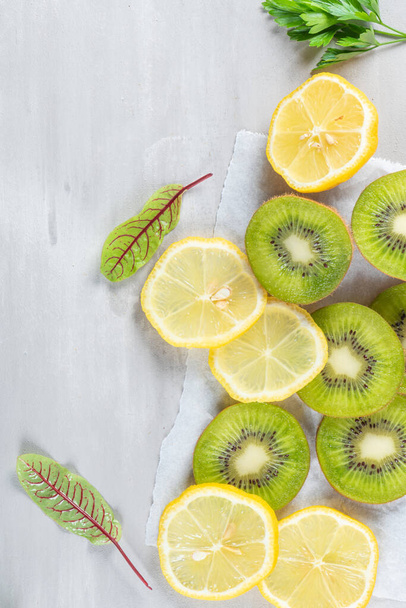 Gesunde Ernährung Hintergrund. Geschnittene Früchte auf grauem Steinhintergrund. Zitrus, Orange, Zitrone, Kiwi, grüne Blätter. Rohkost-Ernährung. - Foto, Bild