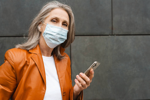 Grey senior woman in face mask using mobile phone outdoors - Valokuva, kuva
