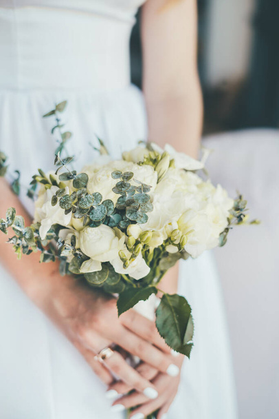 Close-up de um delicado lindo buquê de casamento nas mãos da noiva em um vestido branco
.  - Foto, Imagem