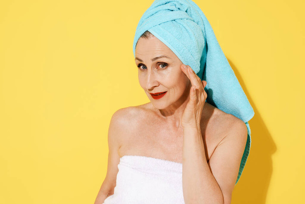 Mature woman wrapped in shower towels looking at camera isolated over yellow wall - Photo, image