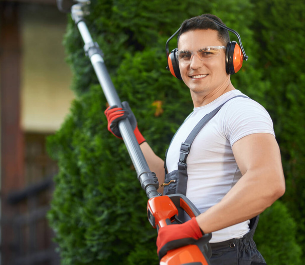 Man in uniform posing at garden with electric hedge trimmer  - Photo, Image
