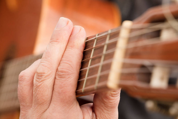 Mano del guitarrista o mano del músico en fa mayor acorde en cuerda de guitarra acústica en suave luz natural en vista lateral - Foto, Imagen