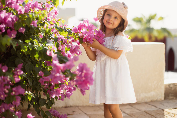 Portrait of a cute and beautiful girl on a background of pink blooming flowers of tropical tree. - Fotografie, Obrázek