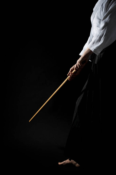Une fille en hakama noir debout dans la pose de combat avec une épée en bois bokken sur fond sombre. Profondeur de champ faible. FSD.  - Photo, image