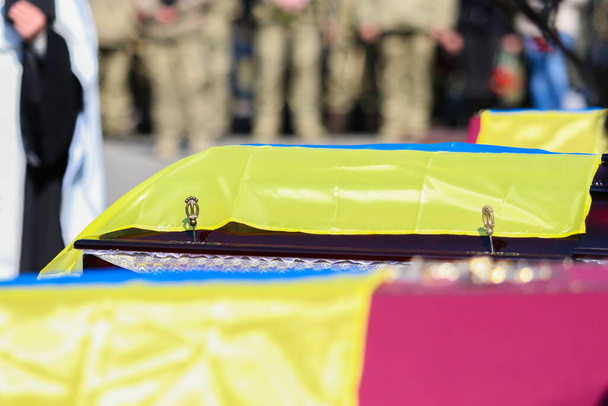 POLTAVA, UKRAINE - MARCH 17, 2022: Red wooden coffins covered with Ukrainian flags with victims of Russian attack on Ukraine during funeral service - Zdjęcie, obraz