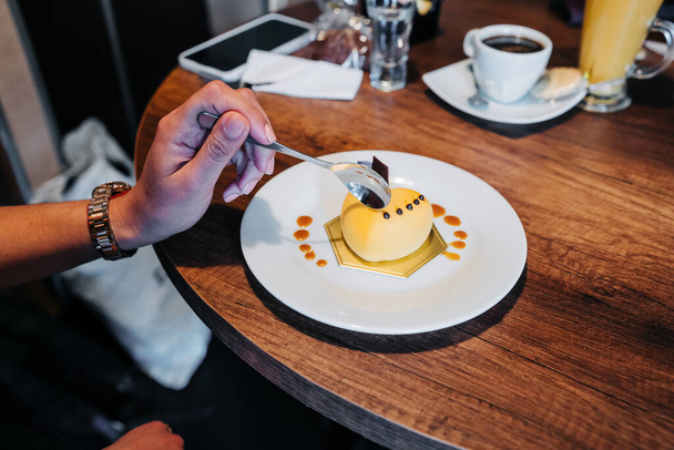 gourmet dessert decorated with icing, person's hand holding spoon and eating, elegant lifestyle, confectionery served on restaurant table - Foto, imagen