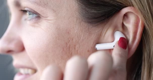 Bezprzewodowe białe słuchawki bluetooth w uchu kobiety - Materiał filmowy, wideo