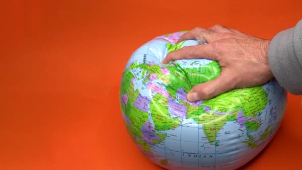 Main dégonflant un globe mondial sur fond orange. - Séquence, vidéo