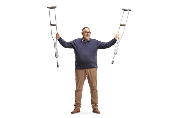 Happy mature man holding crutches up after recovery isolated on white background - Fotoğraf, Görsel
