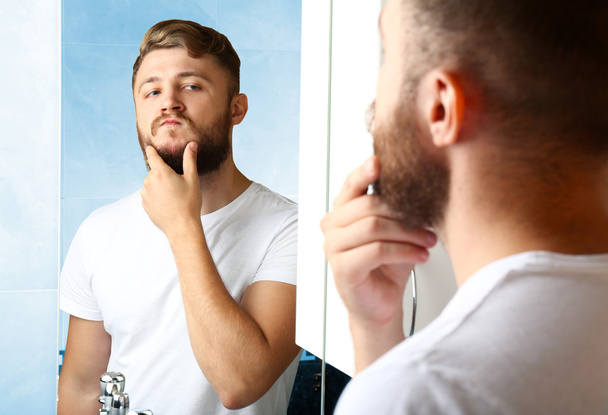 Young man shaving his beard in bathroom - Foto, immagini
