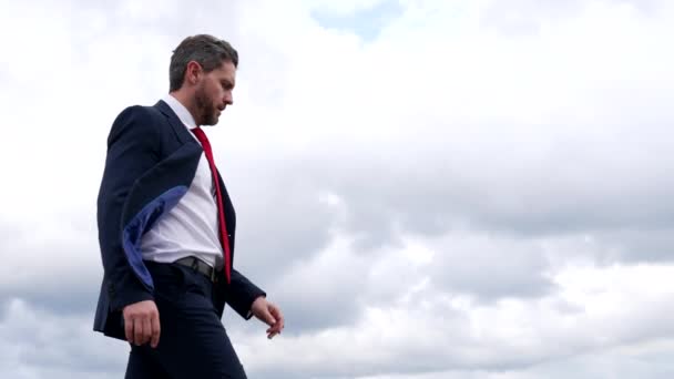 Σοβαρός σκηνοθέτης άνθρωπος με επίσημη κοστούμι έλεγχο ρολόι, ενώ το περπάτημα στο συννεφιασμένο ουρανό, ο χρόνος - Πλάνα, βίντεο