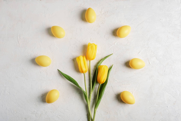 Geel geschilderde eieren en tulpen op witte textuur achtergrond. Pasen concept. Bovenaanzicht, vlak lay - Foto, afbeelding