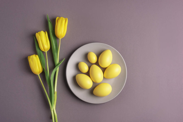 Apparecchiatura della tavola pasquale con piatto grigio, fiori di tulipano giallo e uova sullo sfondo. Vista dall'alto, piatta - Foto, immagini