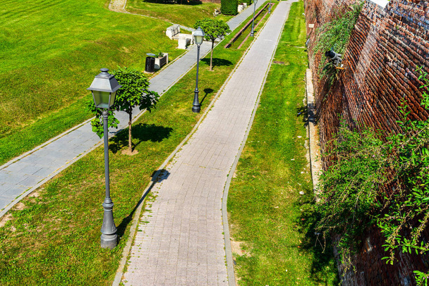 Jardín verde con césped limpio, hermosos árboles, callejones en un patio de la fortaleza. Los muros de fortificación y paseos en Alba Iulia, Rumania, 2021 - Foto, Imagen
