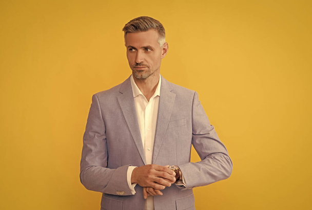 Reifer Mann im sachlichen Anzug checkt Zeit auf gelbem Hintergrund, Zeit - Foto, Bild