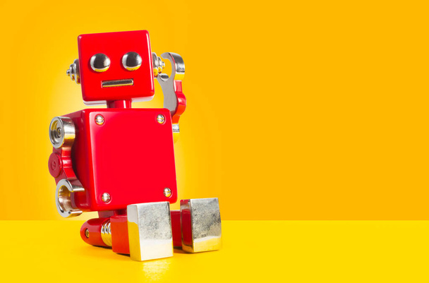 赤い色の昔ながらのレトロな金属製のおもちゃのロボットがオレンジの背景に座っている. - 写真・画像