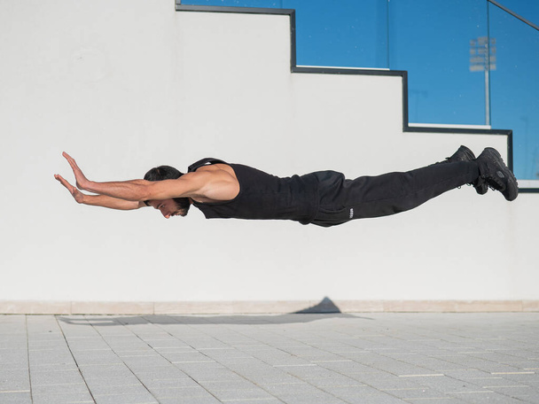 A man in black sportswear jumps while doing push-ups outdoors. - Foto, Imagen