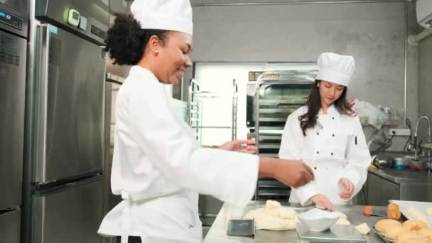 Twee professionele vrouwelijke koks in witte kokkin uniformen en schorten kneden deeg en eieren, bereiden brood, koekjes en vers bakkerijvoedsel, bakken in de oven in een roestvrijstalen keuken van een restaurant. - Video