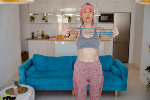 Donna sportiva che utilizza fascia di resistenza del braccio durante l'allenamento a casa - Foto, immagini
