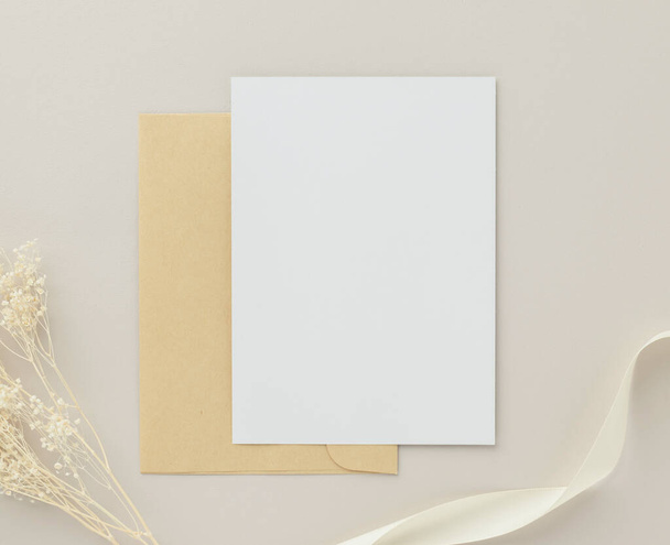 Convite de cartão de saudação em branco Mockup 5x7 no envelope marrom com flores secas no fundo bege, flat lay, mockup - Foto, Imagem