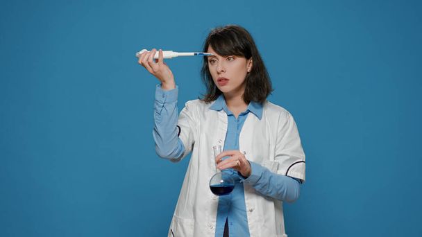 Naistutkija, joka käyttää mikropipettiä nesteen tiputtamiseen dekantterilasiin - Valokuva, kuva