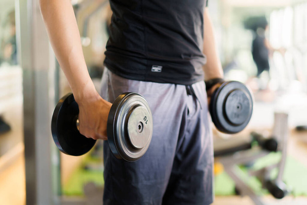 Active Asian sportsman doing a weight exercise in a gym - fitness by lifting up a dumbbell, man sitting on a exercise bench and lift up dumbbells. Sportsman making a shoulder and arms exercise. - Foto, Imagen