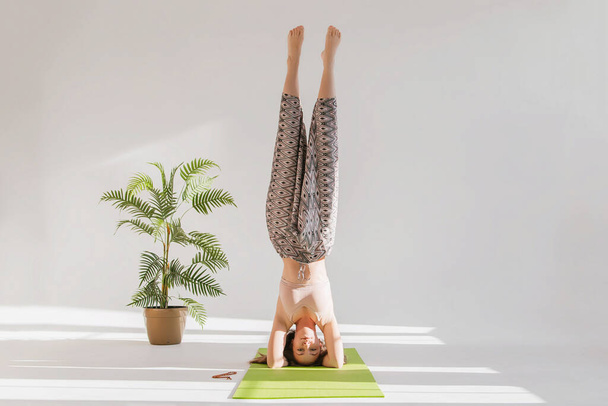 Mulher fazendo ioga em um fundo branco. A menina está de pé em sua cabeça em um quarto brilhante. Estilo de vida saudável - Foto, Imagem