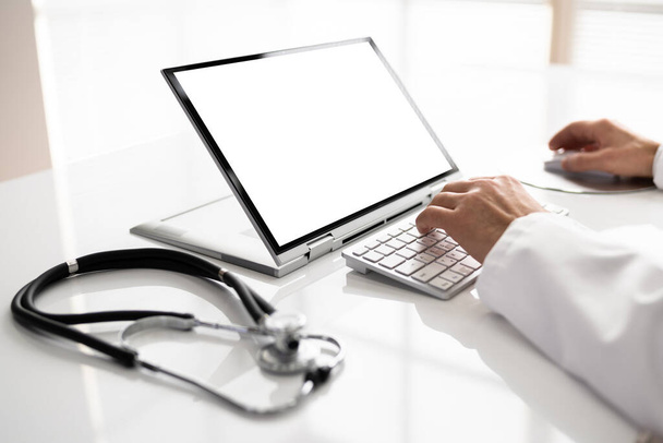 Środek męskiego lekarza korzystającego z laptopa przy biurku w klinice - Zdjęcie, obraz