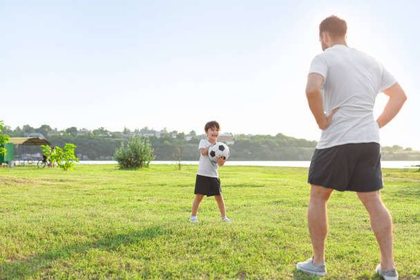 Μικρό αγόρι που παίζει ποδόσφαιρο με τον πατέρα του στο γήπεδο. - Φωτογραφία, εικόνα