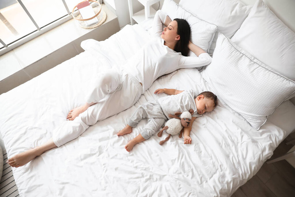 Jonge moeder en haar schattige baby met speelgoed slapen op bed - Foto, afbeelding