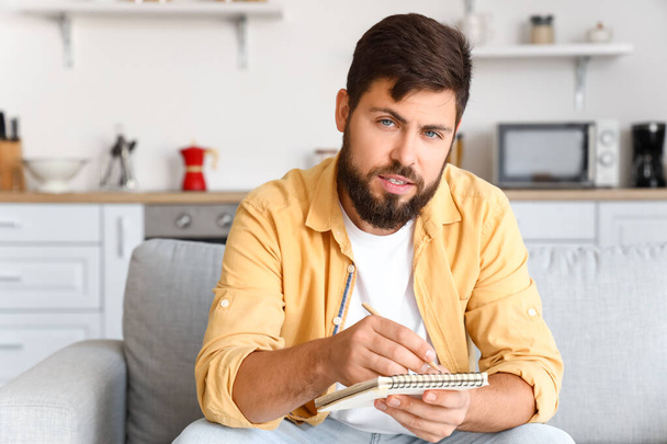 Jóképű férfi jegyzetel, miközben videó chat a konyhában - Fotó, kép