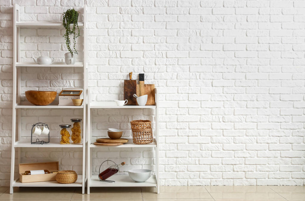 Modernas estanterías con utensilios de cocina cerca de la pared de ladrillo blanco - Foto, Imagen