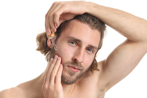 Young man using serum for skin care on white background - Foto, imagen