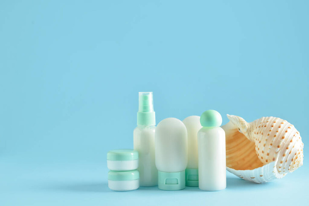 Botellas de viaje, frascos con productos cosméticos y concha marina sobre fondo azul - Foto, Imagen