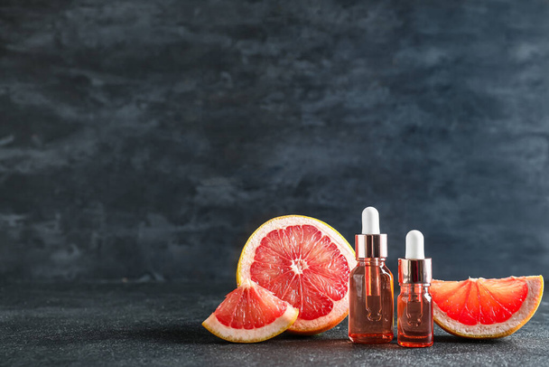 Bottles with essential oil and ripe grapefruit on dark background - Photo, Image