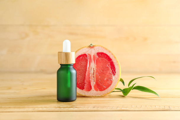 Flasche mit ätherischem Öl und der Hälfte der Grapefruit auf Holzgrund - Foto, Bild